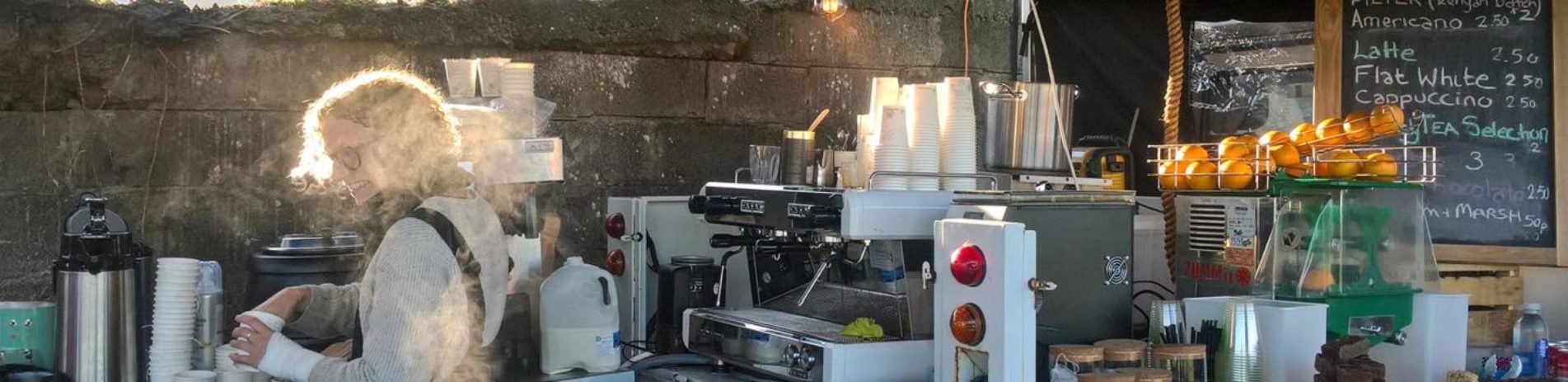 lady-with-glasses-smiling-and-preparing-coffee-behind-coffee-bar-with-coffee-machinery-and-price-list-on-chalk-board-at-forth-valley-food-fest