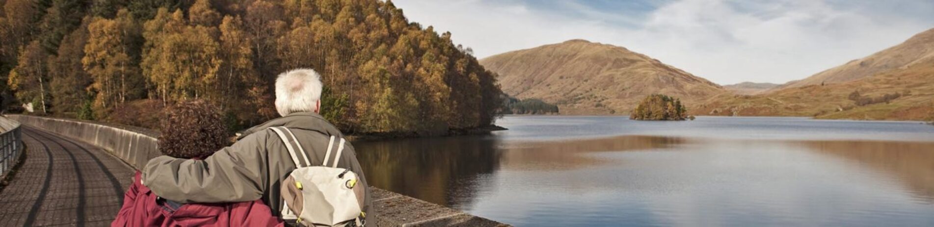 older-couple-holding-each-other-close-admiring-autumn-views-over-glen-finglas-reservoir