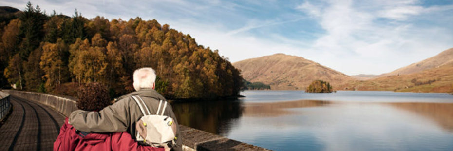 older-couple-looking-out-over-glen-finglas-resevoir-with-autumnal-trees-on-the-left