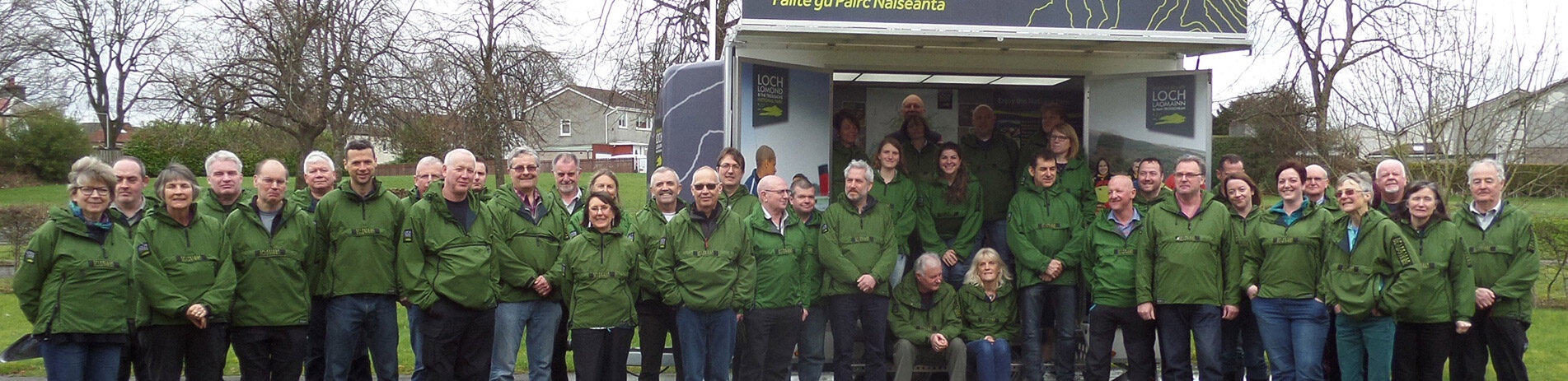 group-of-over-twenty-volunteers-in-green-national-park-jackets-smiling-and-posing