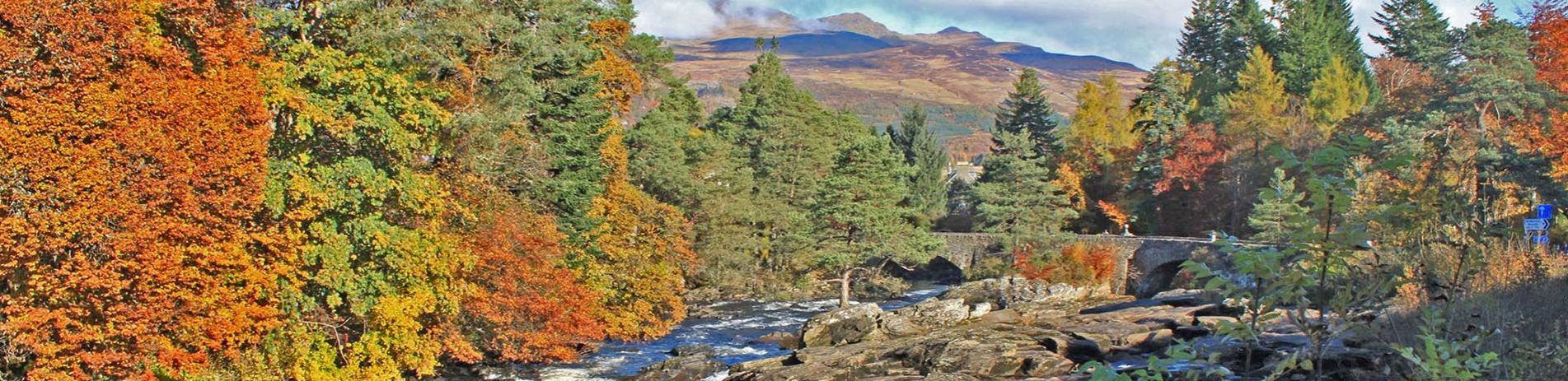 falls-of-dochart-and-ancient-bridge-surrounded-by-trees-in-autumn-colours-with-high-mountains-in-the-distance