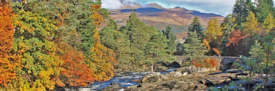 falls-of-dochart-and-ancient-bridge-surrounded-by-trees-in-autumn-colours-with-high-mountains-in-the-distance