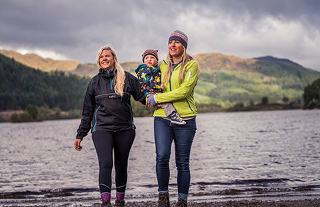 two-women-on-a-loch-shore-holding-small-child-all-smiling
