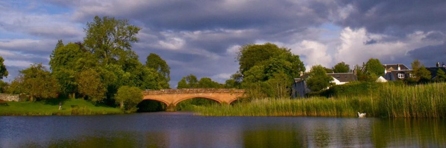 orange-redstone-bridge-over-river-in-calendar-with-cloudy-sky-and buildings-peeking-out-behind-trees-on-either-side