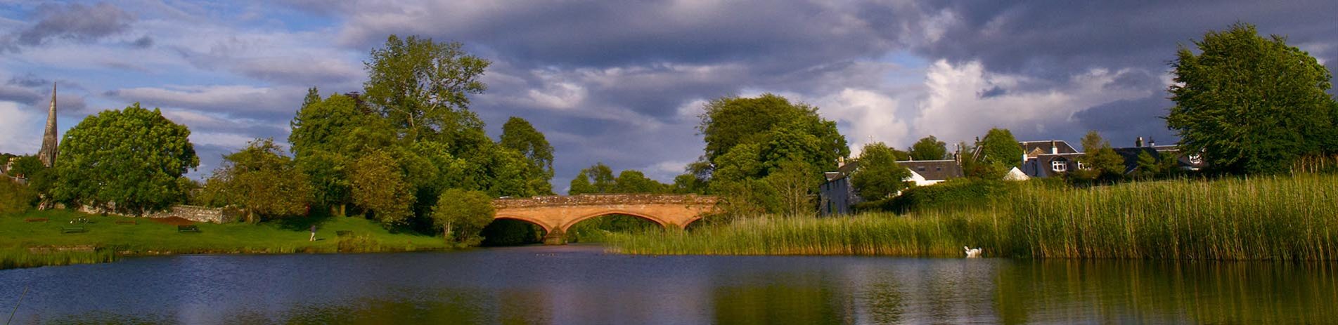 orange-redstone-bridge-over-river-in-calendar-with-cloudy-sky-and buildings-peeking-out-behind-trees-on-either-side