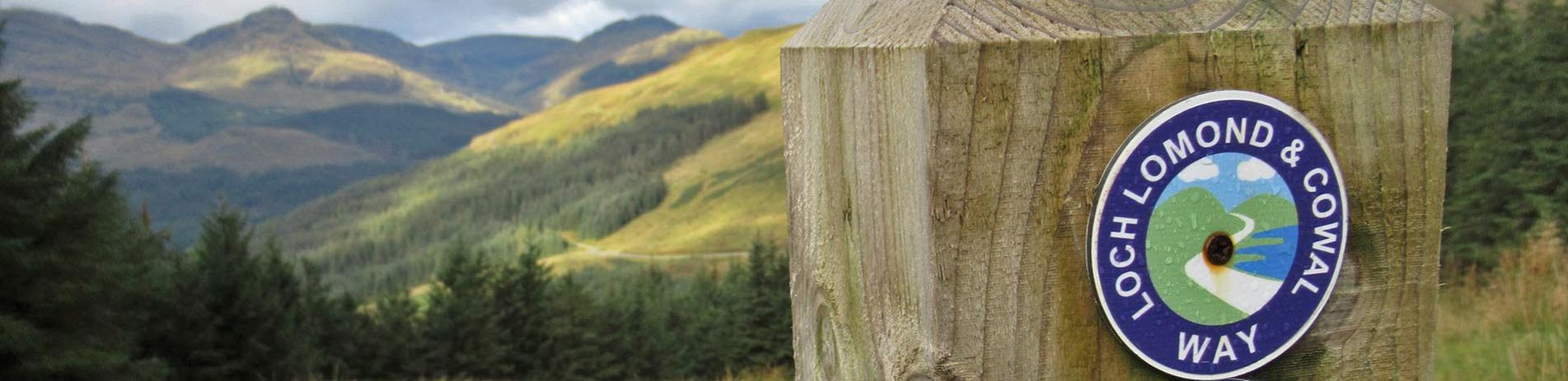 loch-lomond-and-cowal-way-sign-on-wooden-post-with-mountains-and-coniferous-forests-in-the-background