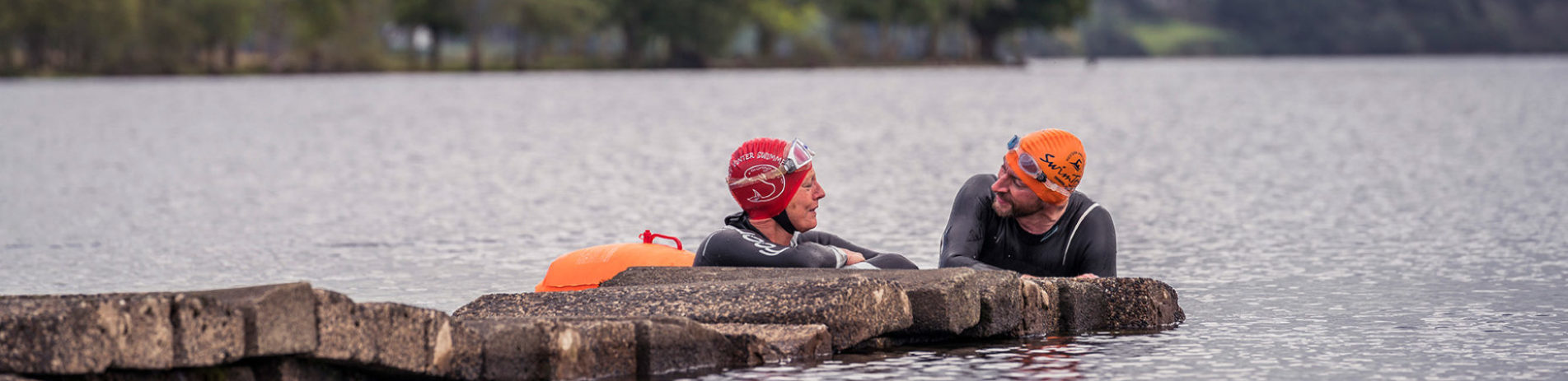 couple-wearing-wet-suits-resting-on-pier-in-the-loch
