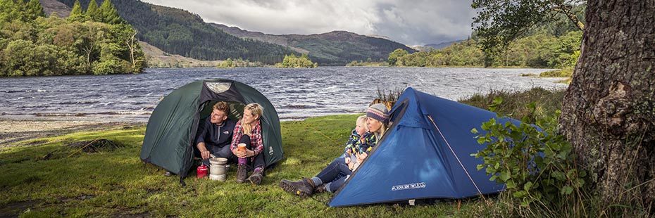 group-of-campers-on-shore-of-loch-chon-bright-sunny-day-couple-cooking-on-left-and-mother-and-baby-on-right