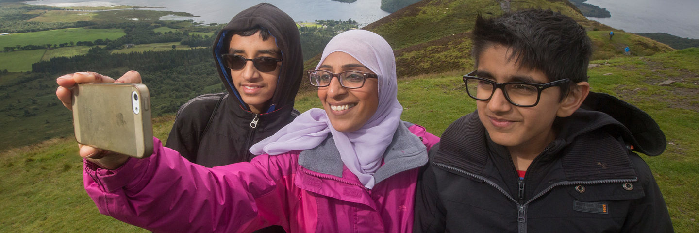 three-young-people-two-boys-and-a-girl-taking-a-selfie-from-the-top-of-conic-hill-overlooking-loch-lomond