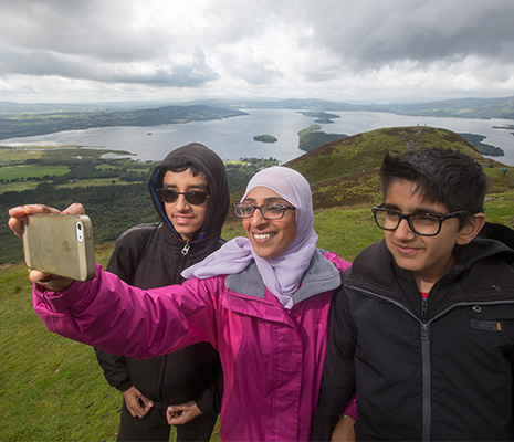 three-young-people-two-boys-and-a-girl-taking-a-selfie-from-the-top-of-conic-hill-overlooking-loch-lomond