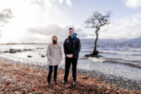 Two people stand next to each other with a windy Loch Lomond in the background