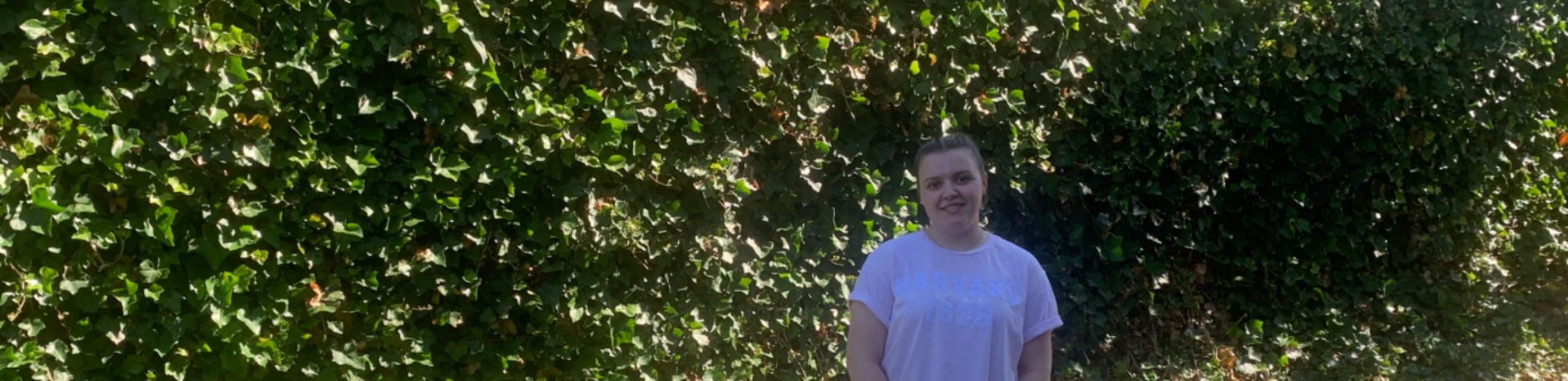 Communications Assistant Iona Brownell standing in front of greenery