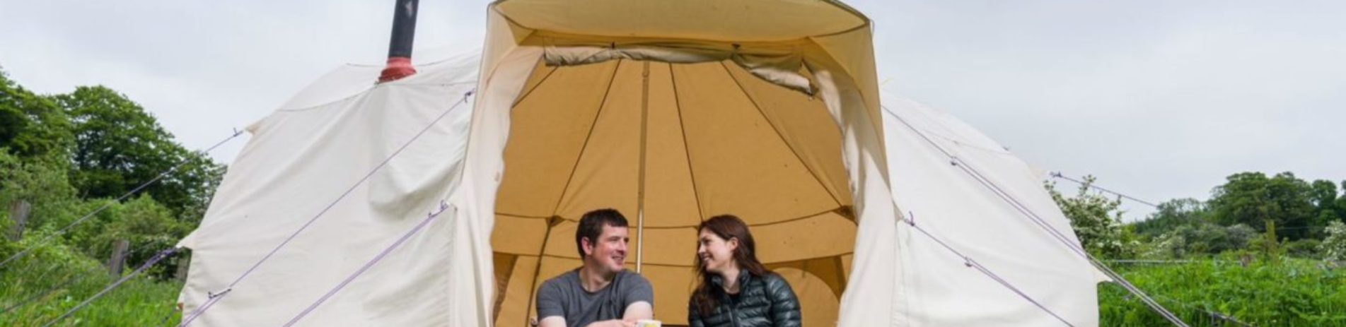 Two people sitting at an open bell tent on Portnellan Farm