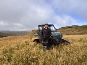 Person standing beside a digger on a hillside