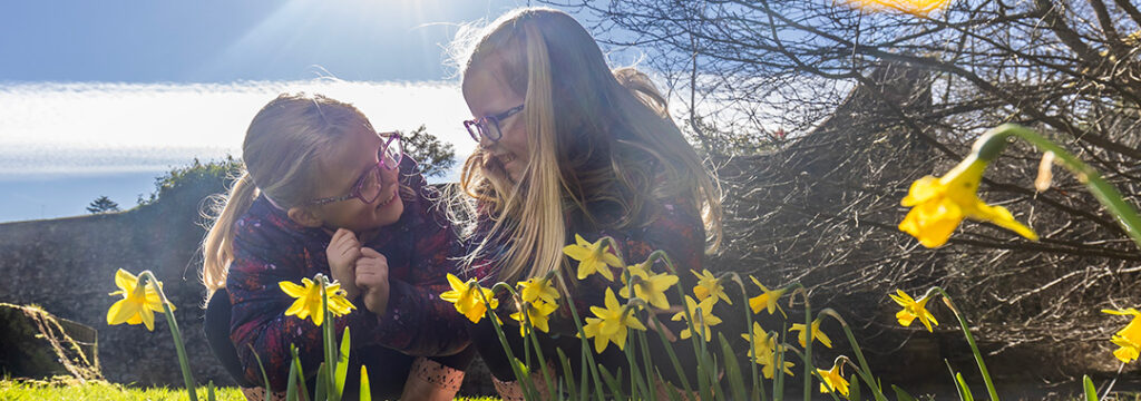 Two children crouching down on grass, surrounded by daffodils 