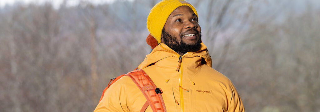 A man dresses in an outdoor jacket, smiling enjoying the outdoors