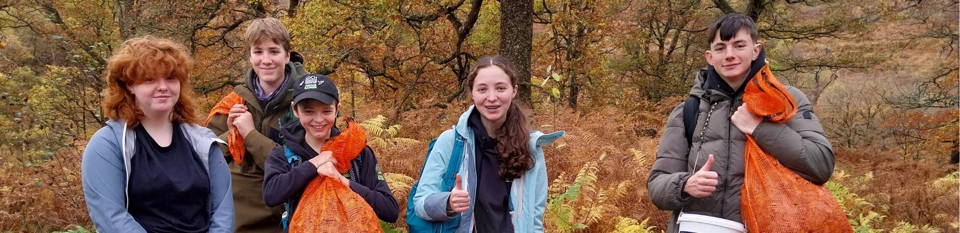 A group of young people in nature holding orange trash bags